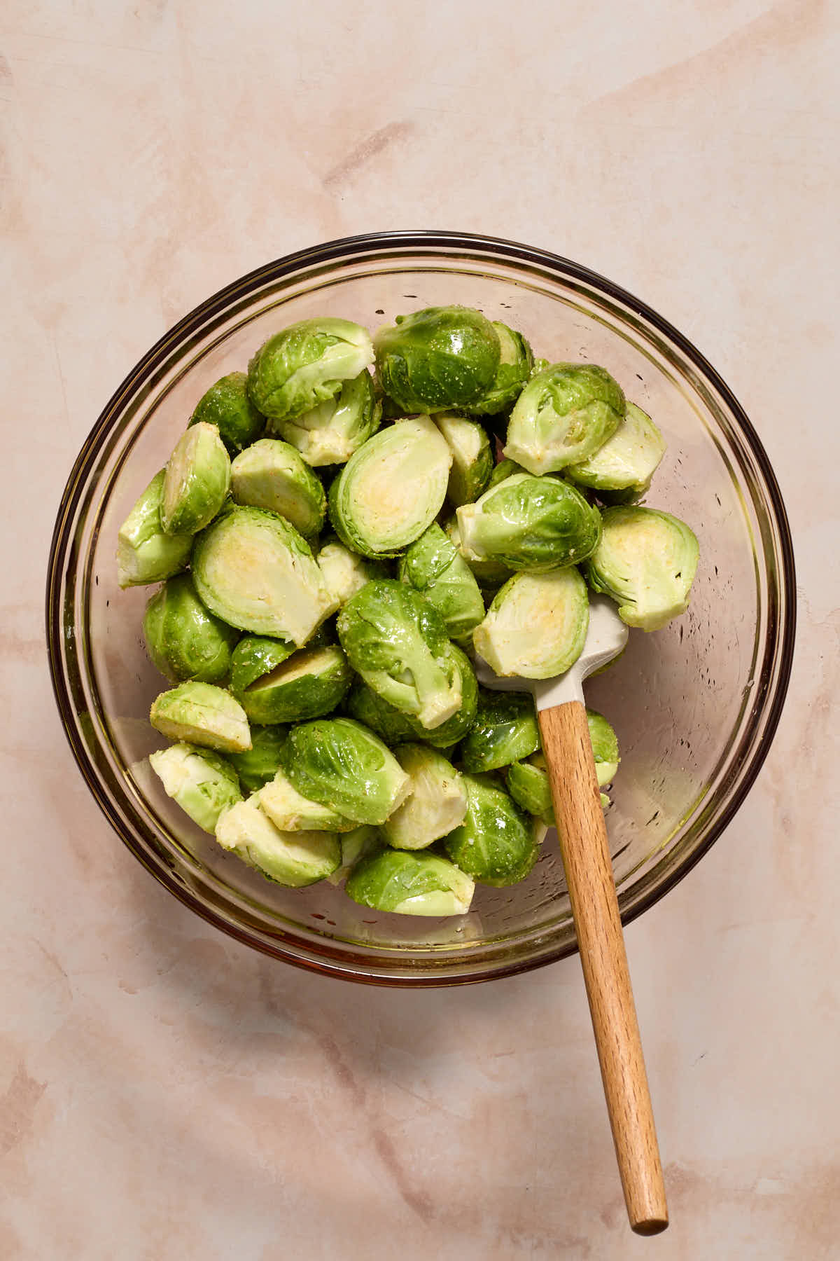 Brussels sprouts cut in half and tossed with oil and seasoning in a glass bowl.