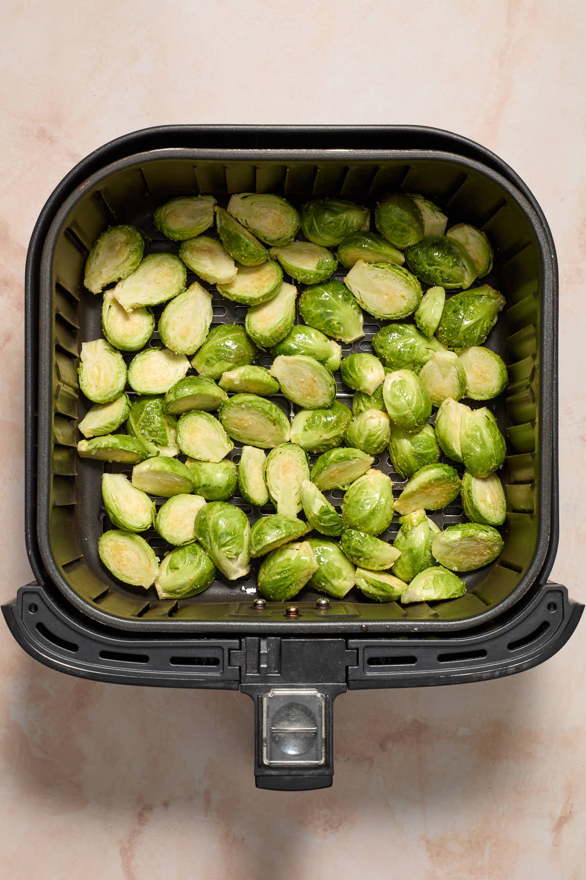 Seasoned Brussels sprouts in an air fryer basket.