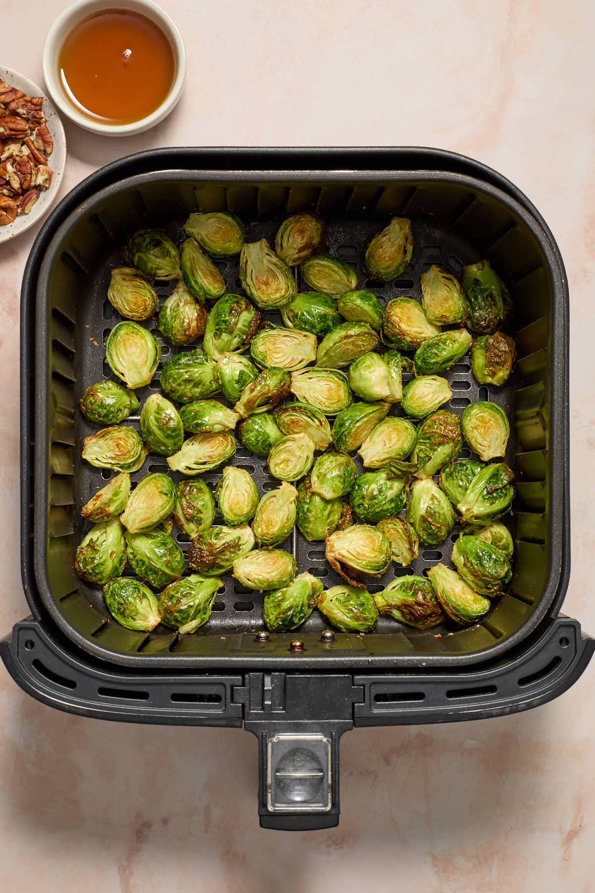 Air fried Brussels sprouts in the basket with chopped pecans and maple syrup on the side.
