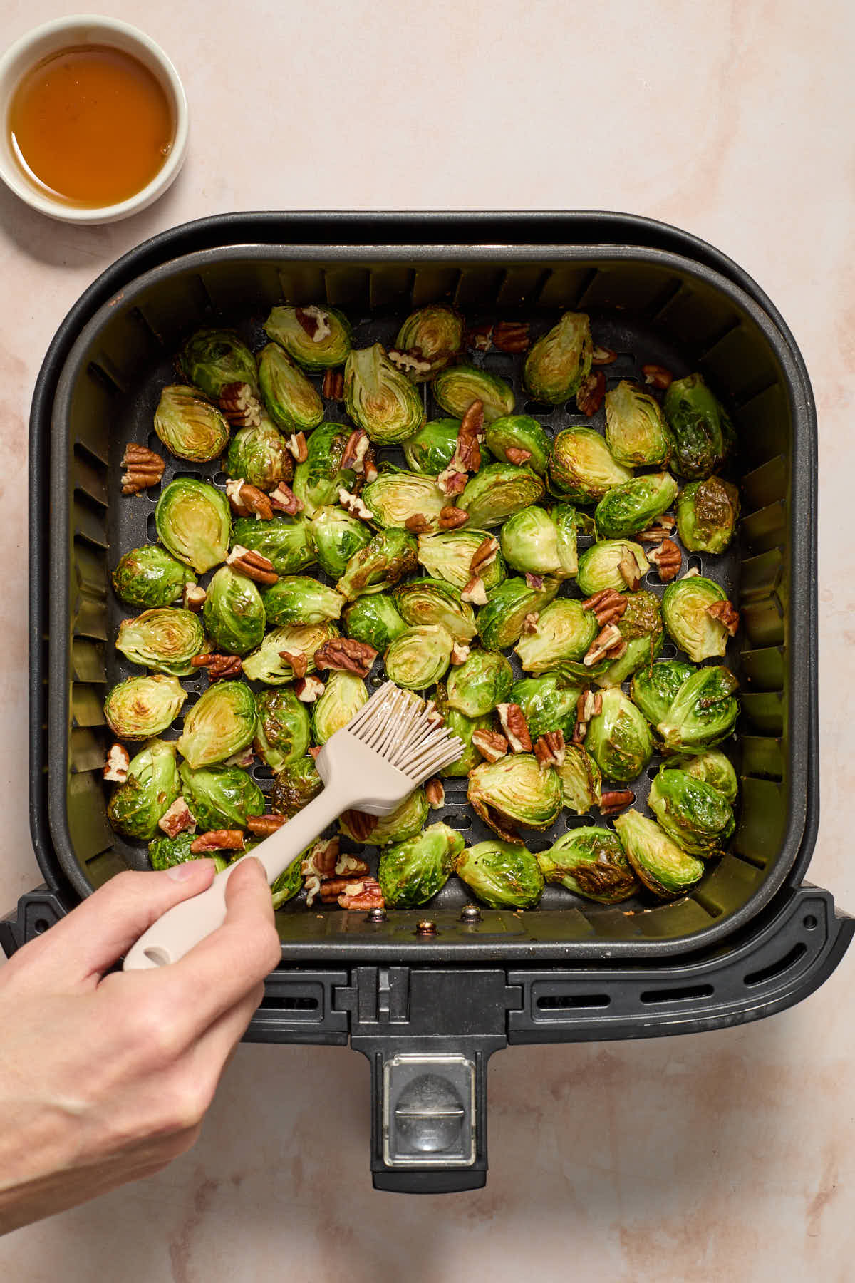 Pecans added to the Brussels sprouts in the air fryer basket with maple syrup being brushed on.