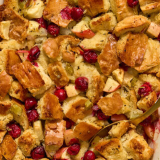 Close up view of baked apple cranberry stuffing with a serving spoon inserted into it.