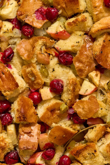 Close up view of baked apple cranberry stuffing with a serving spoon inserted into it.