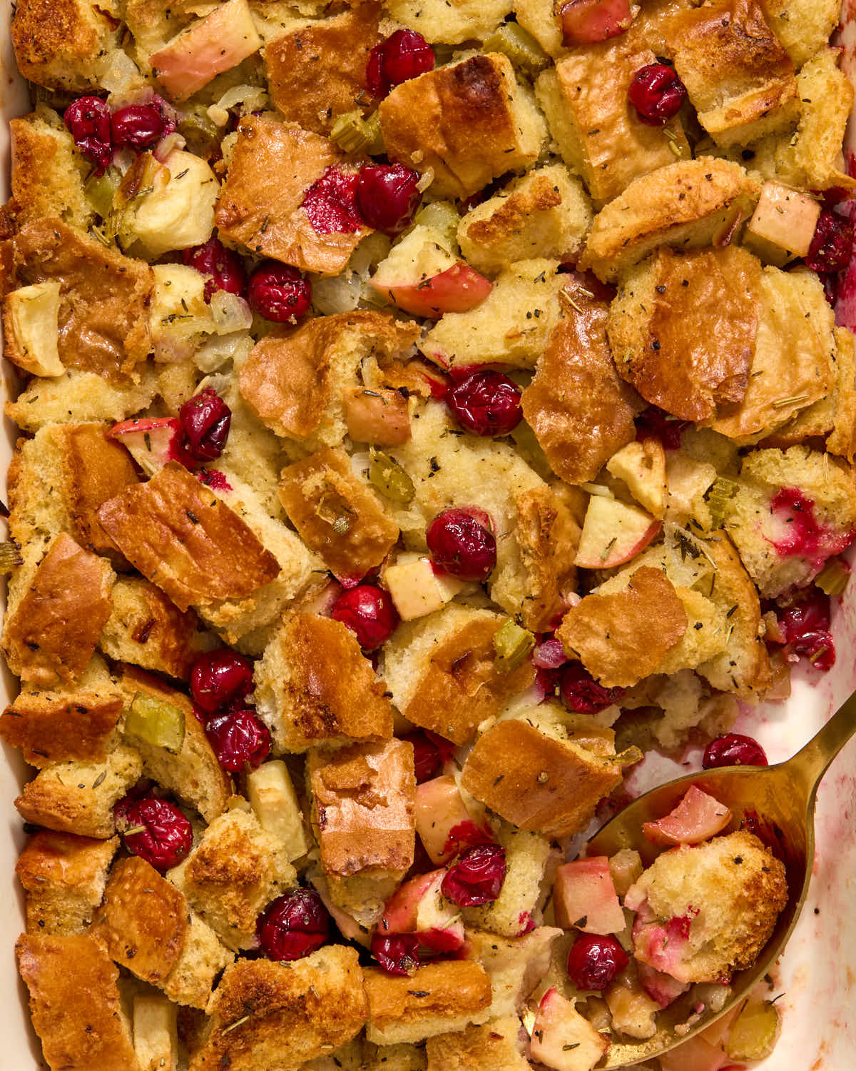 Close up of apple cranberry stuffing in a dish with a spoon inserted into it.