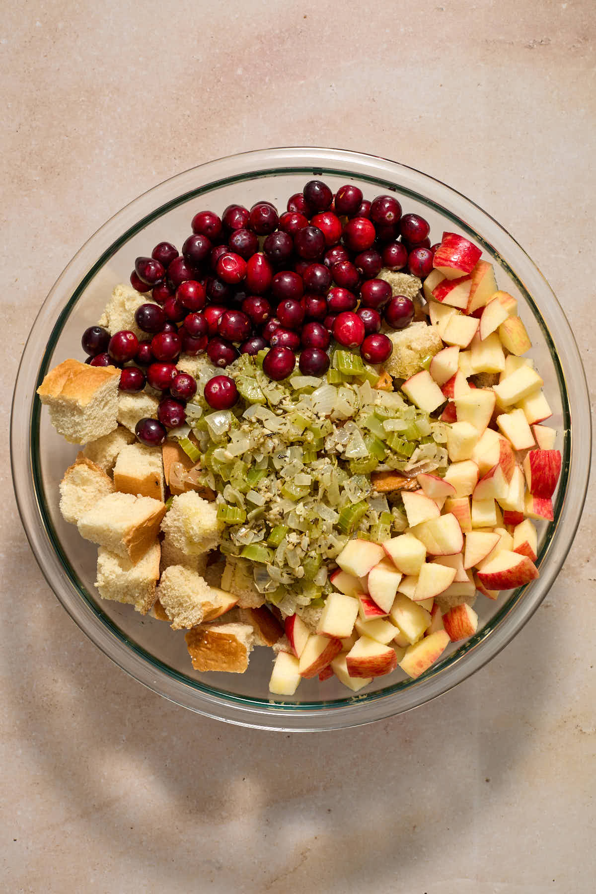 Bread cubes, vegetable mixture, chopped apples and cranberries added to a large glass bowl.