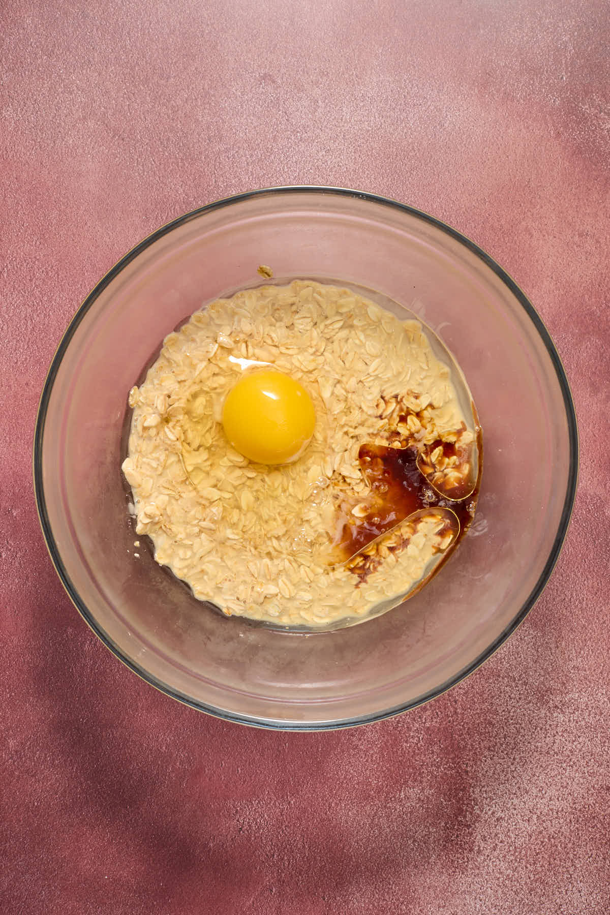 Eggs, oil, vanilla and sugar added to the oat/eggnog mixture in a glass bowl.