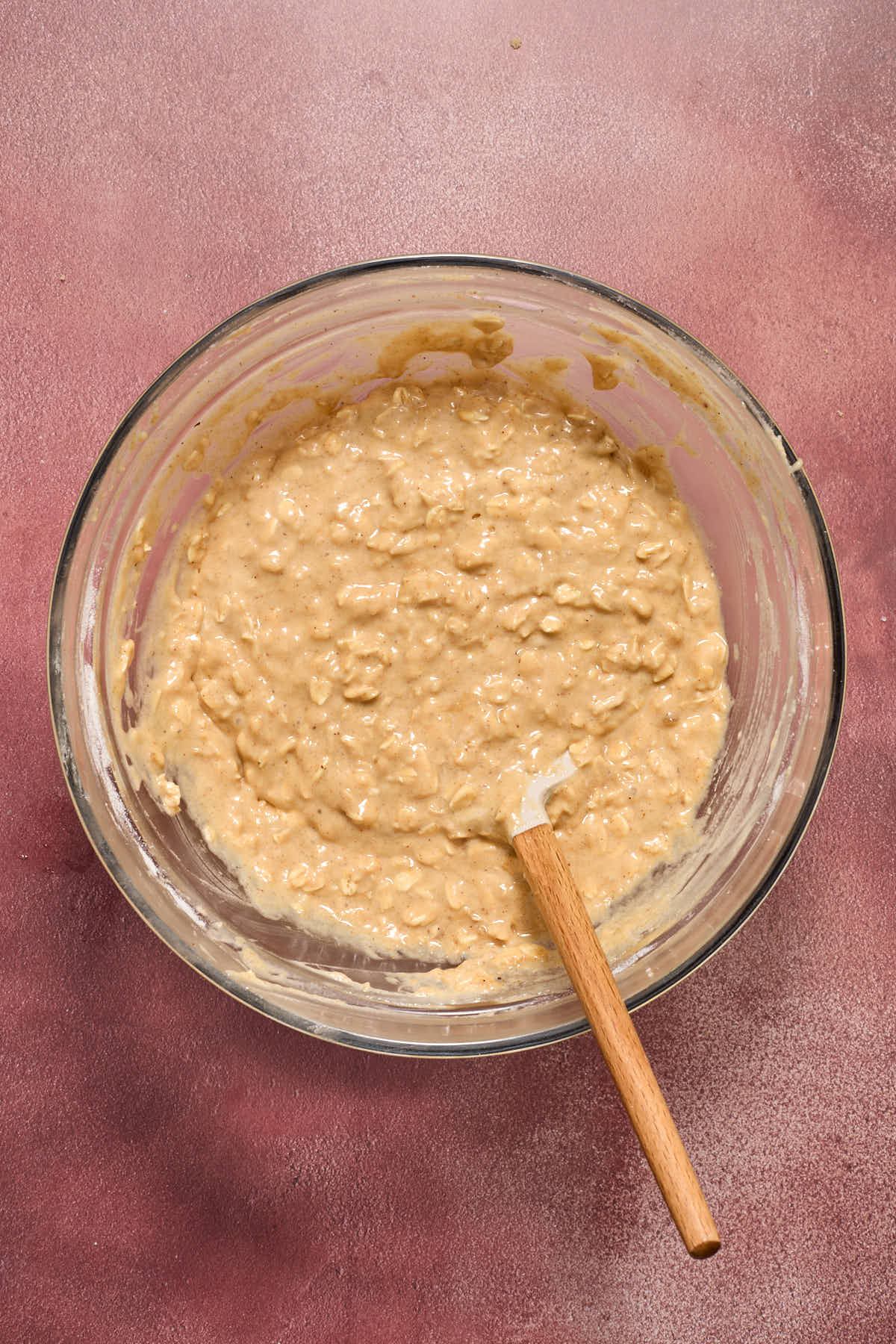 Muffin batter mixed together in a glass bowl with a spatula inserted into it.