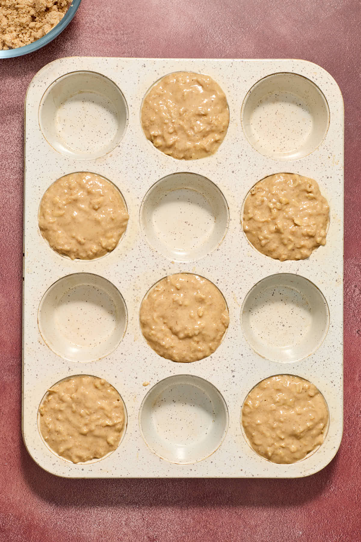 Batter spooned into every second muffin cup in a 12 cup muffin tin.