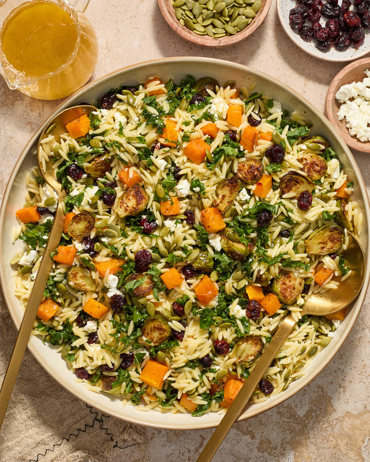 Close up of orzo salad in a large bowl with serving spoons inserted into it.