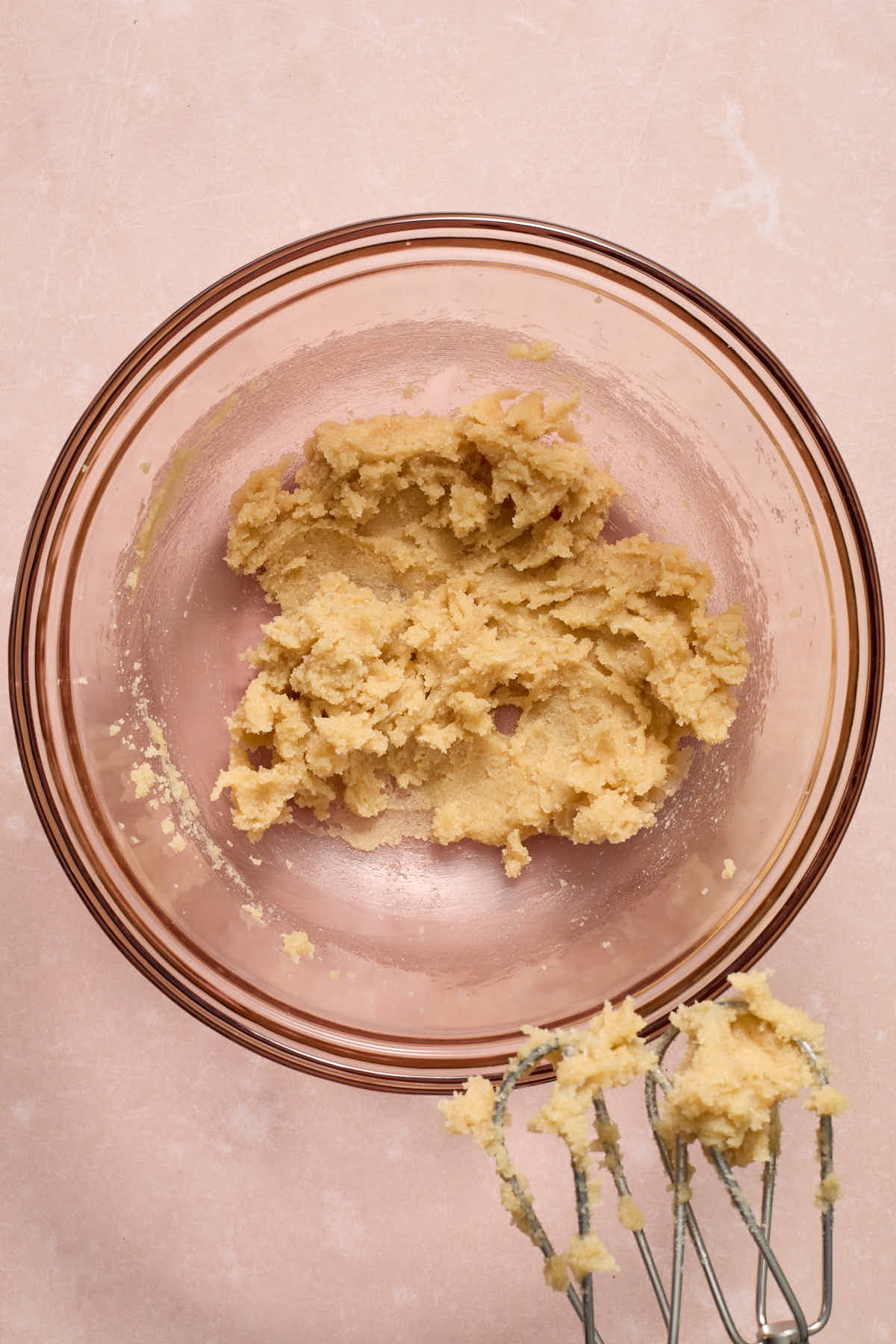 Butter and sugars creamed together in a glass bowl with the beaters in the frame.