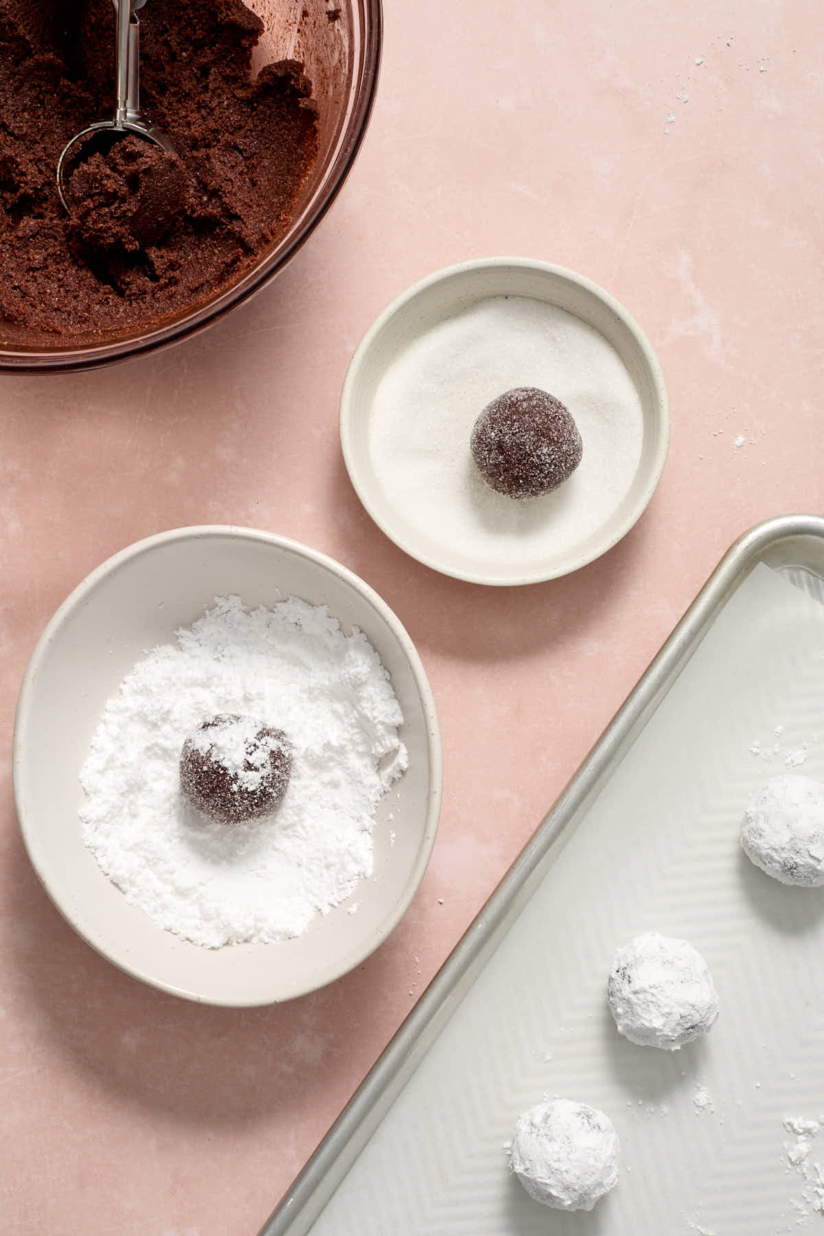 Dough rolled into balls and rolled in a bowl of granulated sugar and then a bowl of powdered sugar.