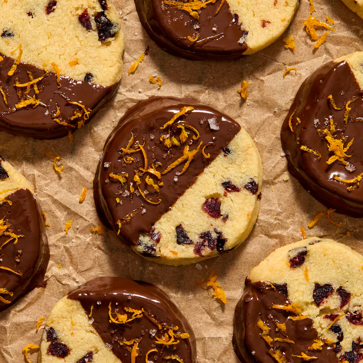Overhead view of almond flour orange cranberry cookies dipped in chocolate and topped with orange zest and flaky sea salt.