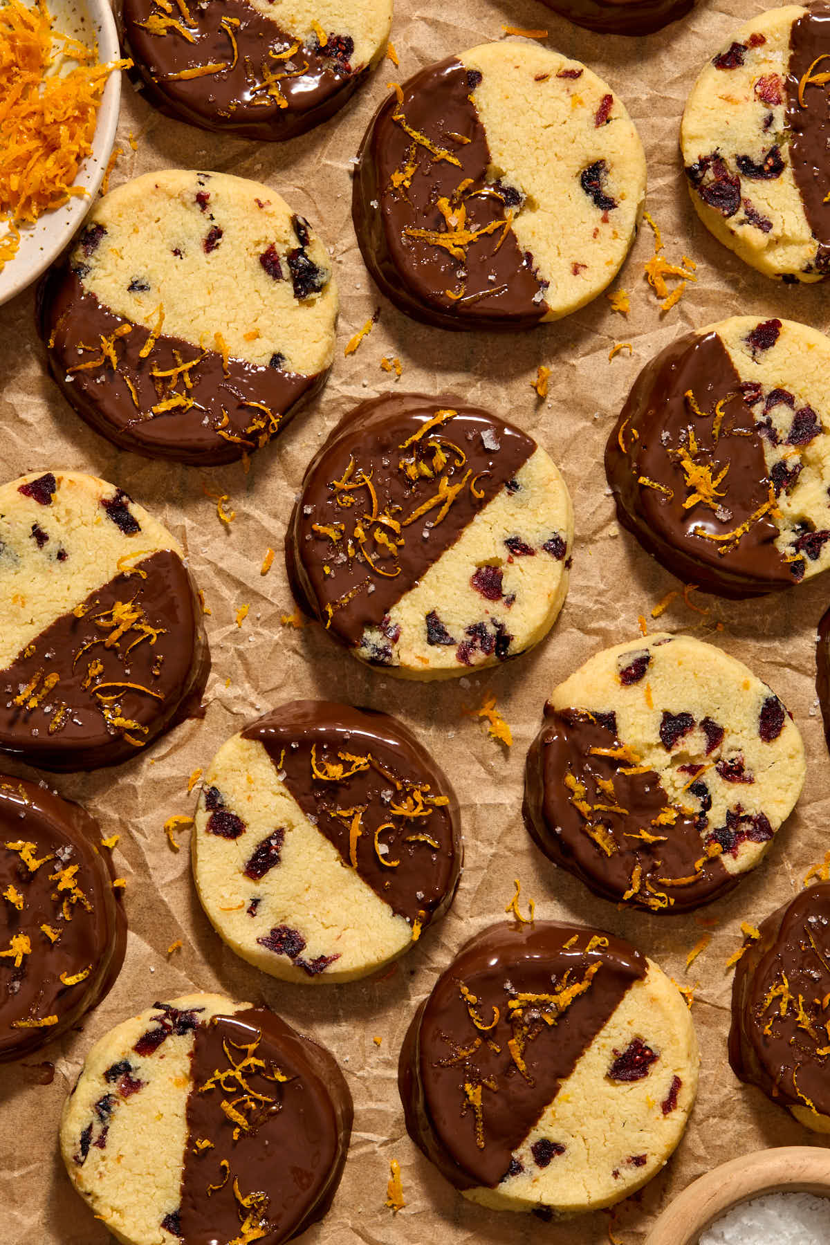 Overhead of cookies on crumpled parchment paper, dipped in chocolate and topped with sea salt and orange zest.