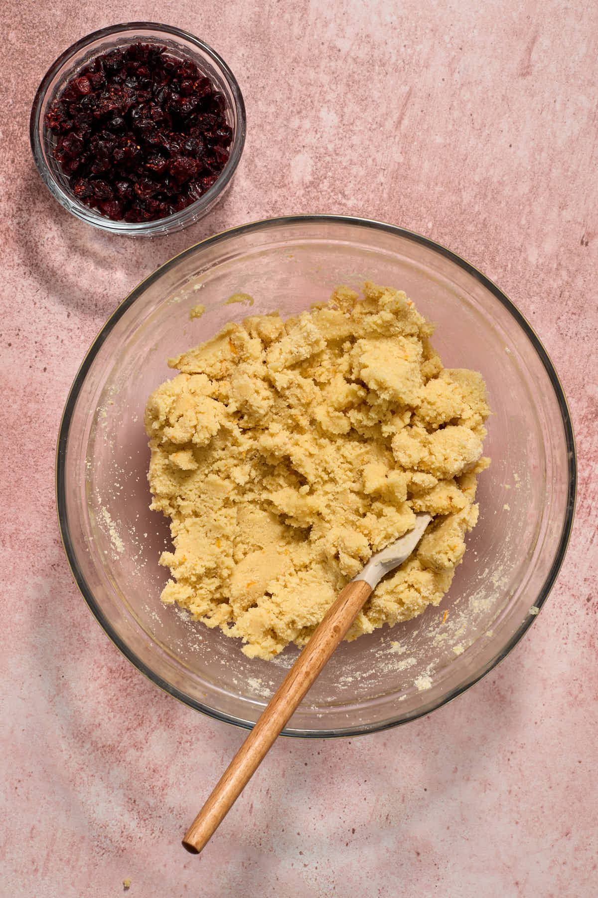 Cookie dough mixed together in a bowl with a spatula inserted into it and chopped dried cranberries on the side.