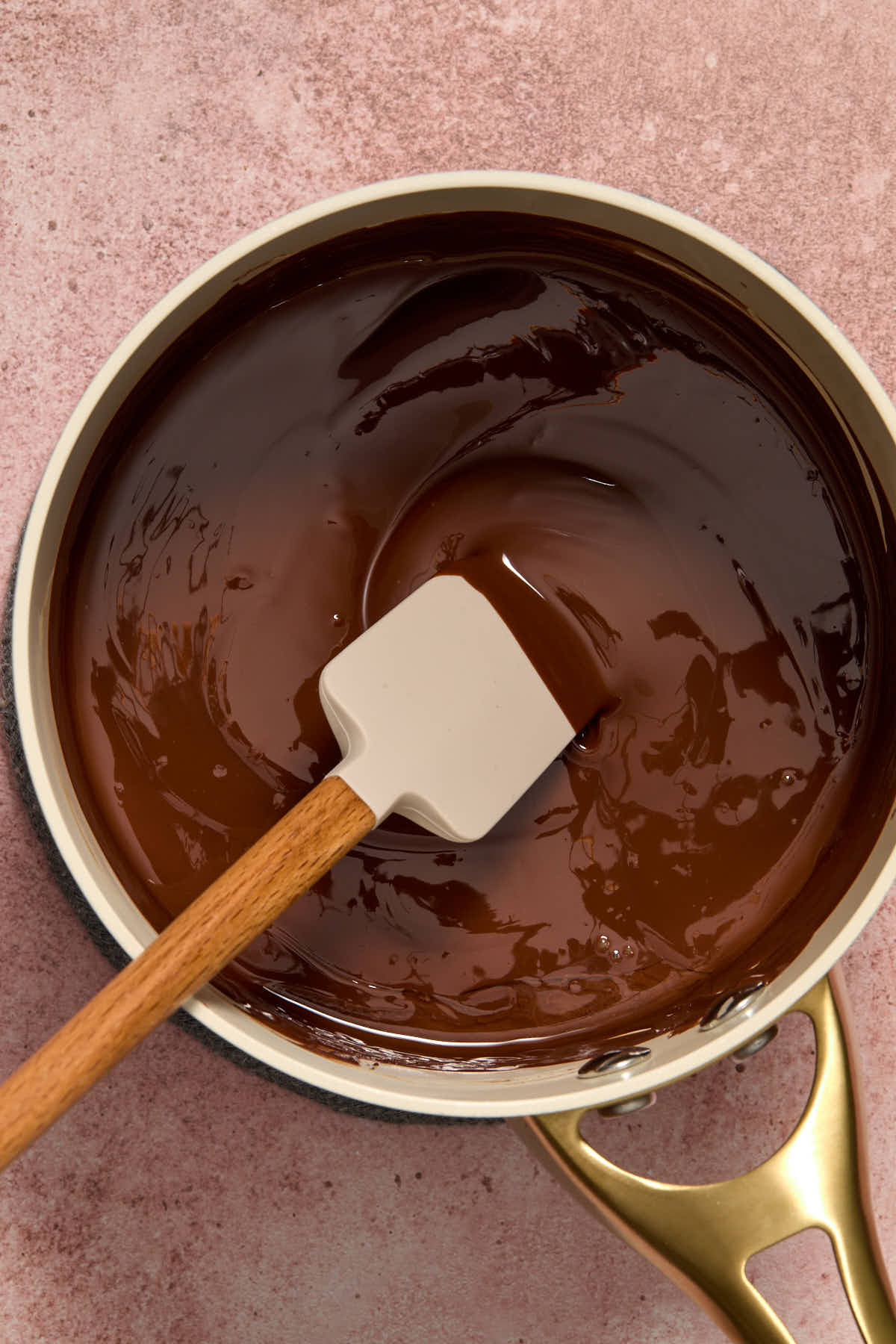 Melted dark chocolate in a small sauce pan with a spatula inserted into it.