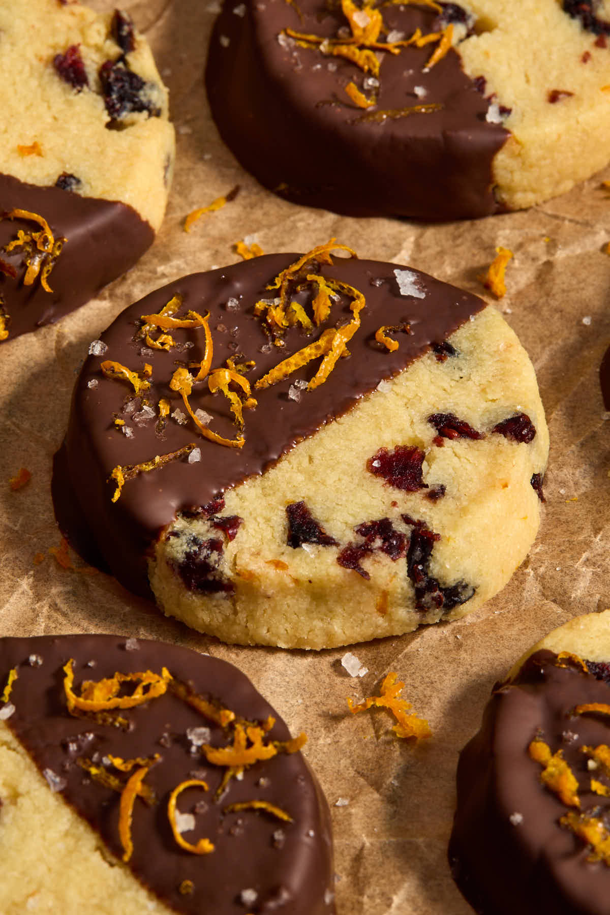 Side view of a chocolate dipped cookie on parchment with other cookies surrounding it.
