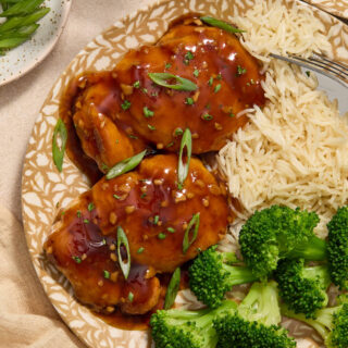 Two air fryer boneless skinless chicken thighs covered in honey garlic sauce on a plate with green onion on top.