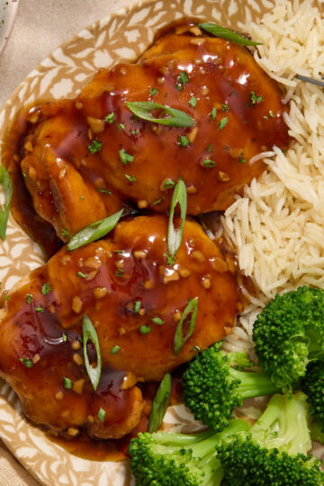 Two air fryer boneless skinless chicken thighs covered in honey garlic sauce on a plate with green onion on top.