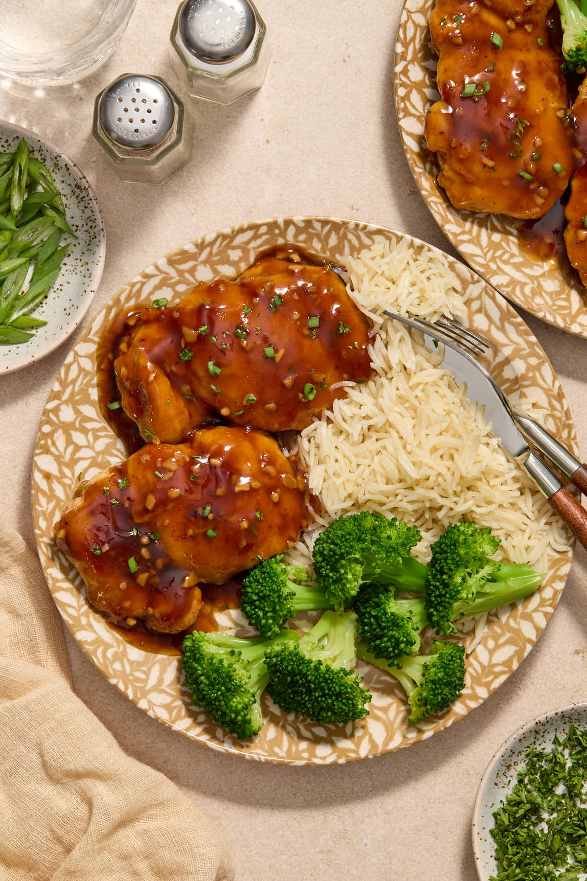 Sauce covered chicken thighs served on plates with rice and broccoli.
