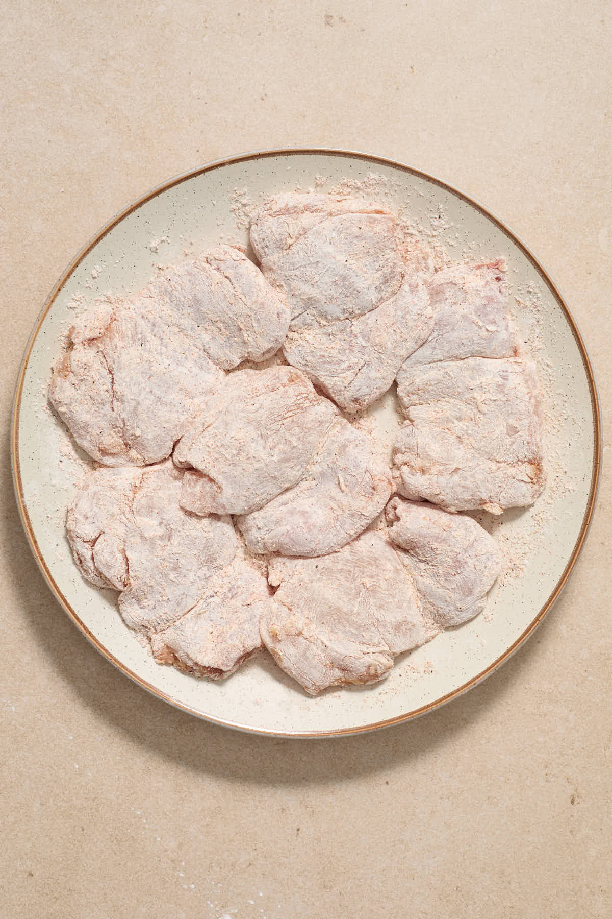 Boneless skinless chicken thighs coated in cornstarch on a plate.