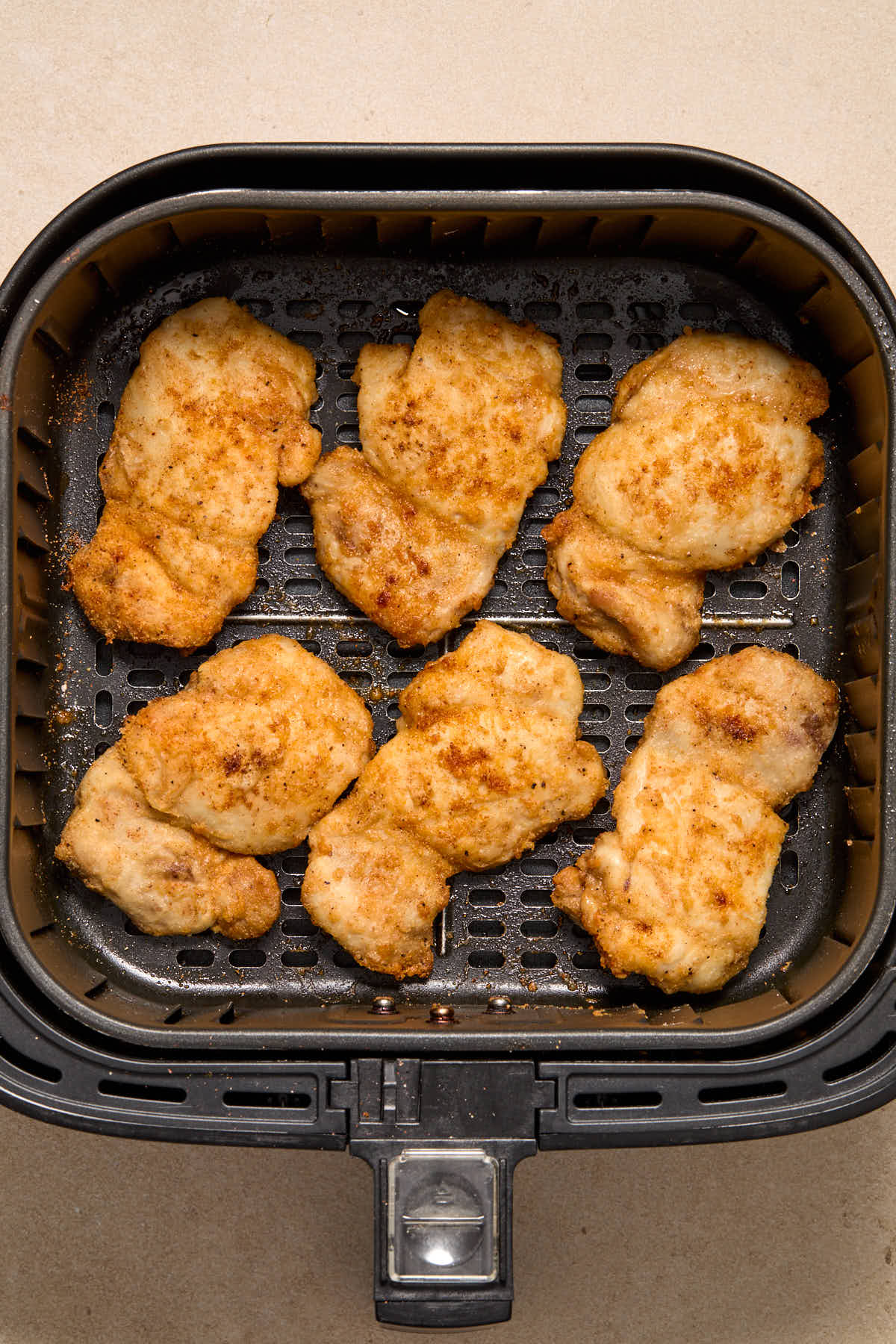 Six air fried boneless skinless chicken thighs in an air fryer basket.