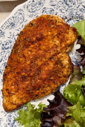 An air fryer chicken cutlet with no breading served on a plate with a green salad on the side.
