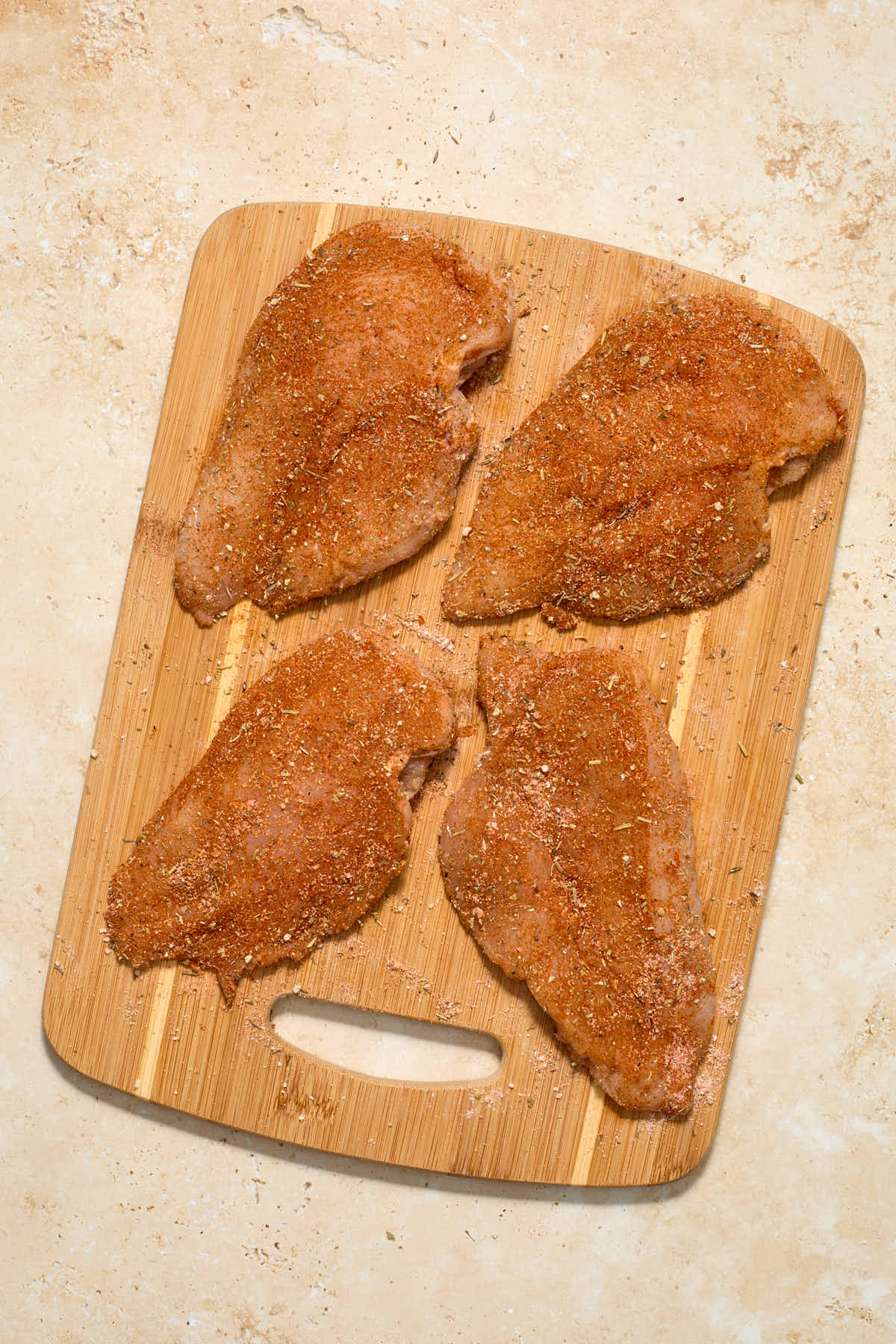 Seasoned chicken cutlets on a wooden cutting board.