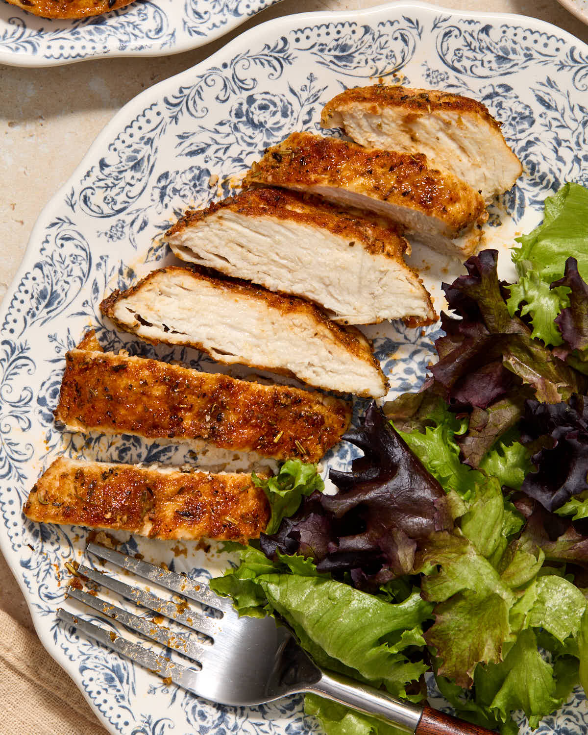 An air fried chicken cutlet sliced on a plate with a green salad on the side.
