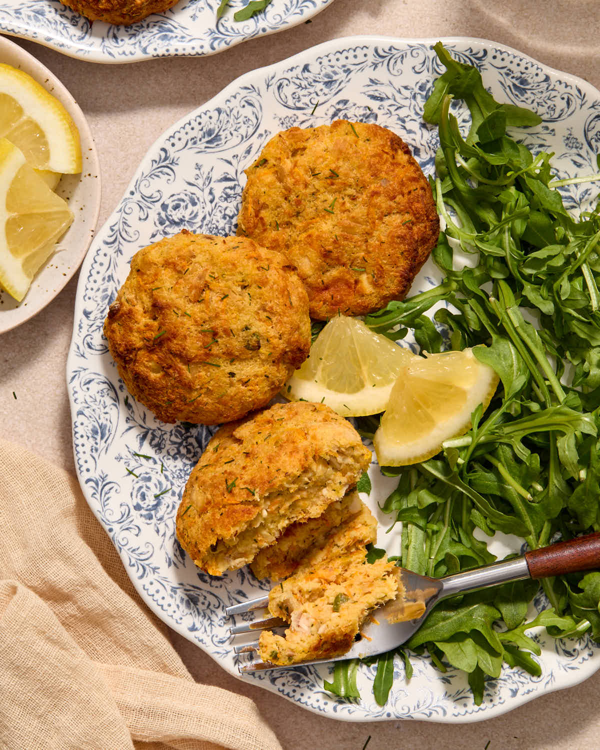 Tuna cakes served on a plate with lemon wedges and greens.