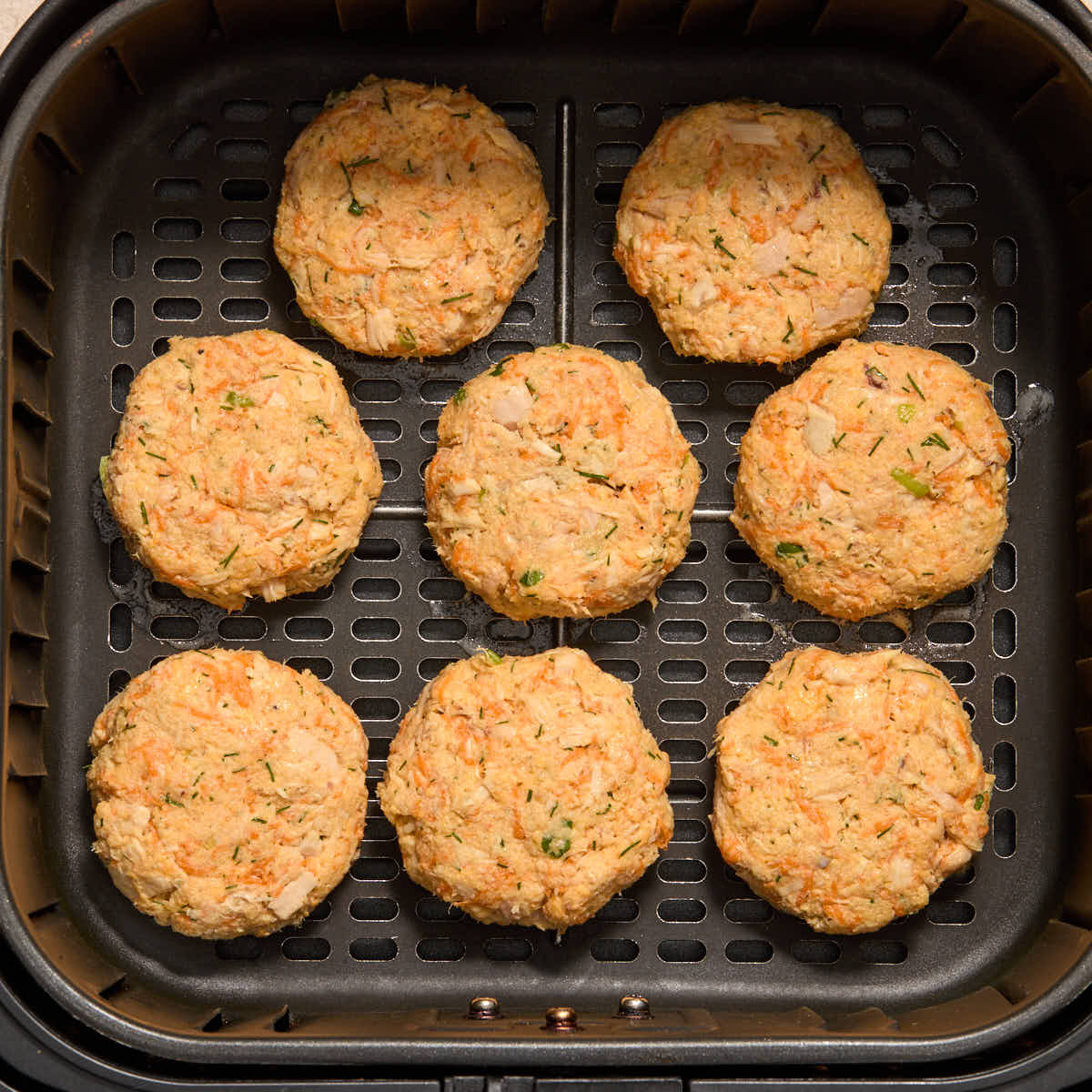 Shaped patties arranged in a single layer in an air fryer basket.