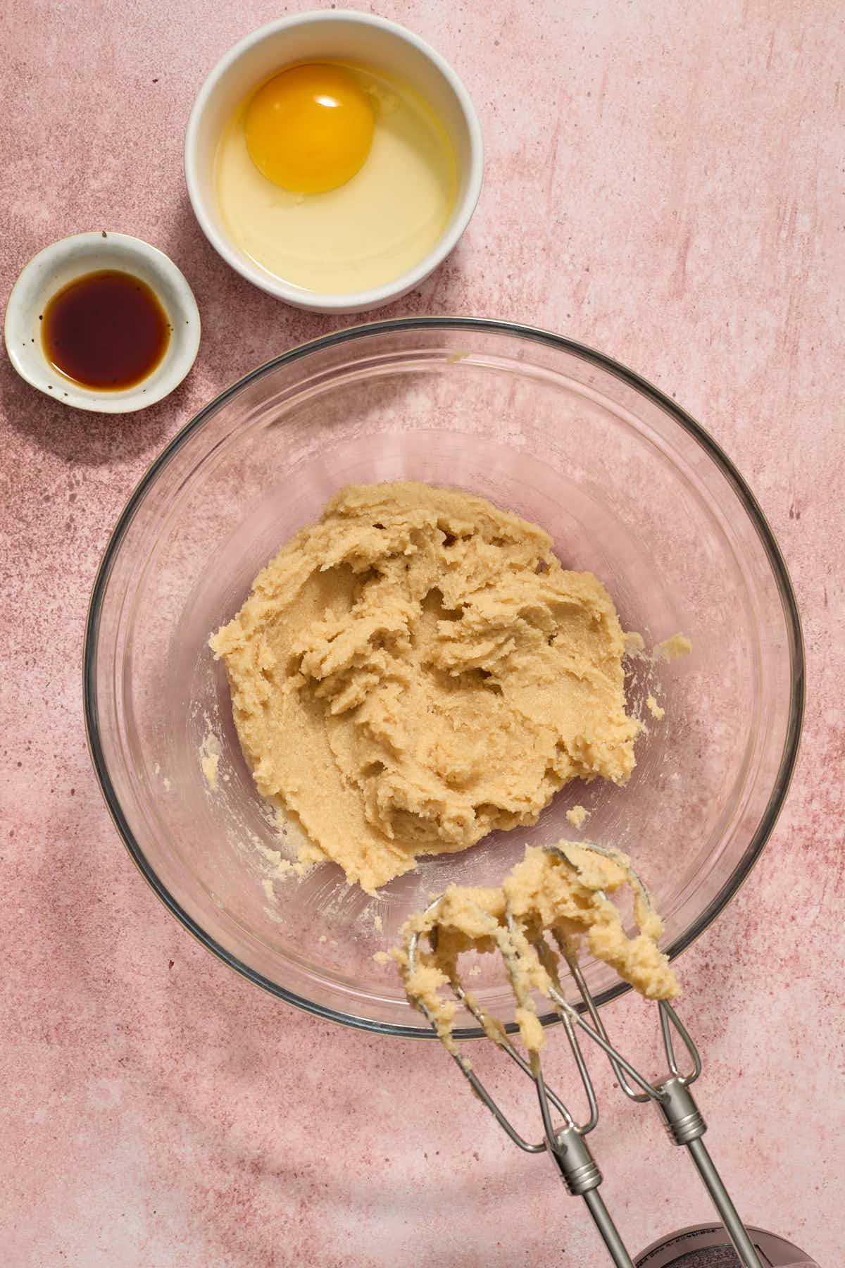 Butter and sugars creamed together in a glass bowl with egg and vanilla off to the side.