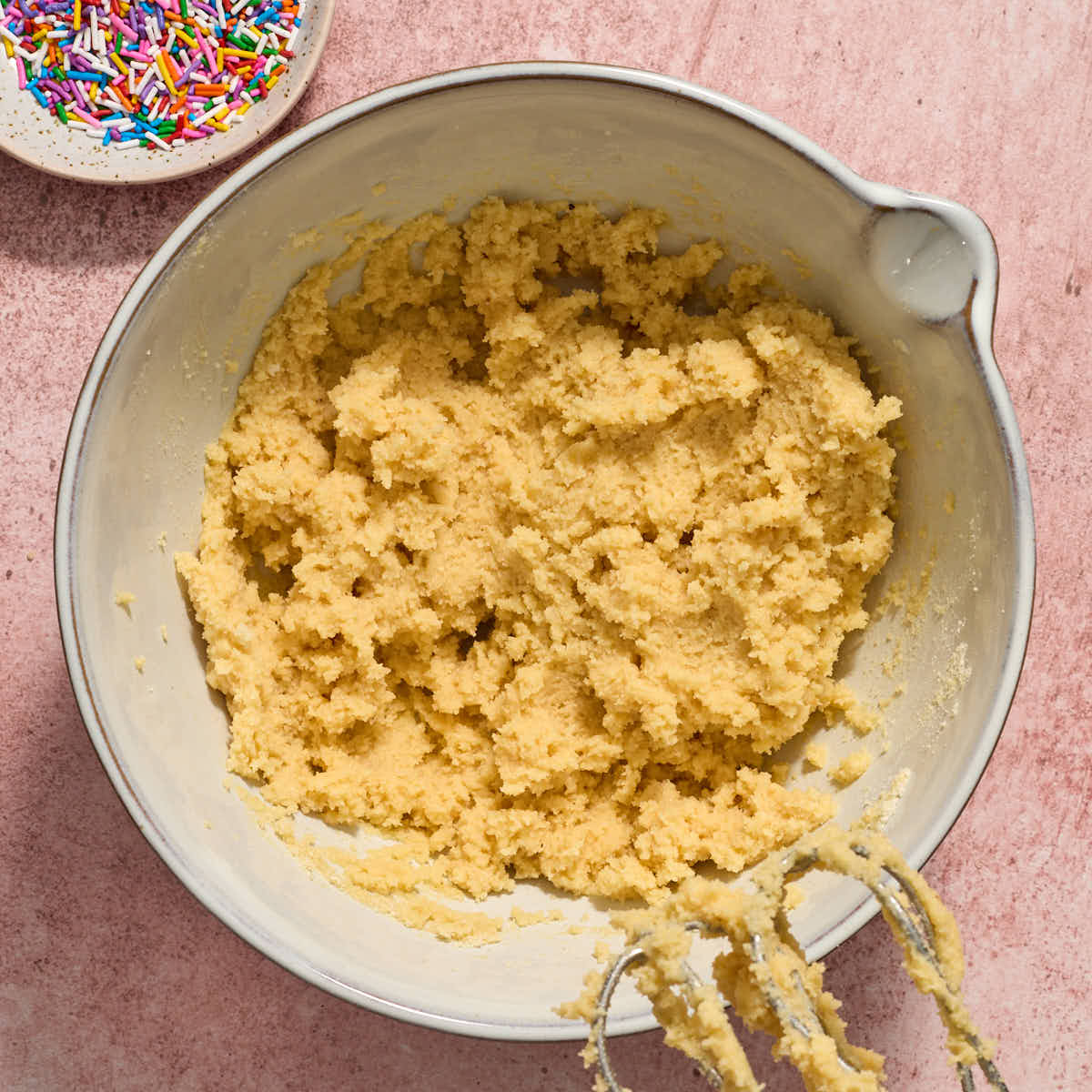 Cookie dough batter in a white bowl with a dish of sprinkles on the side.