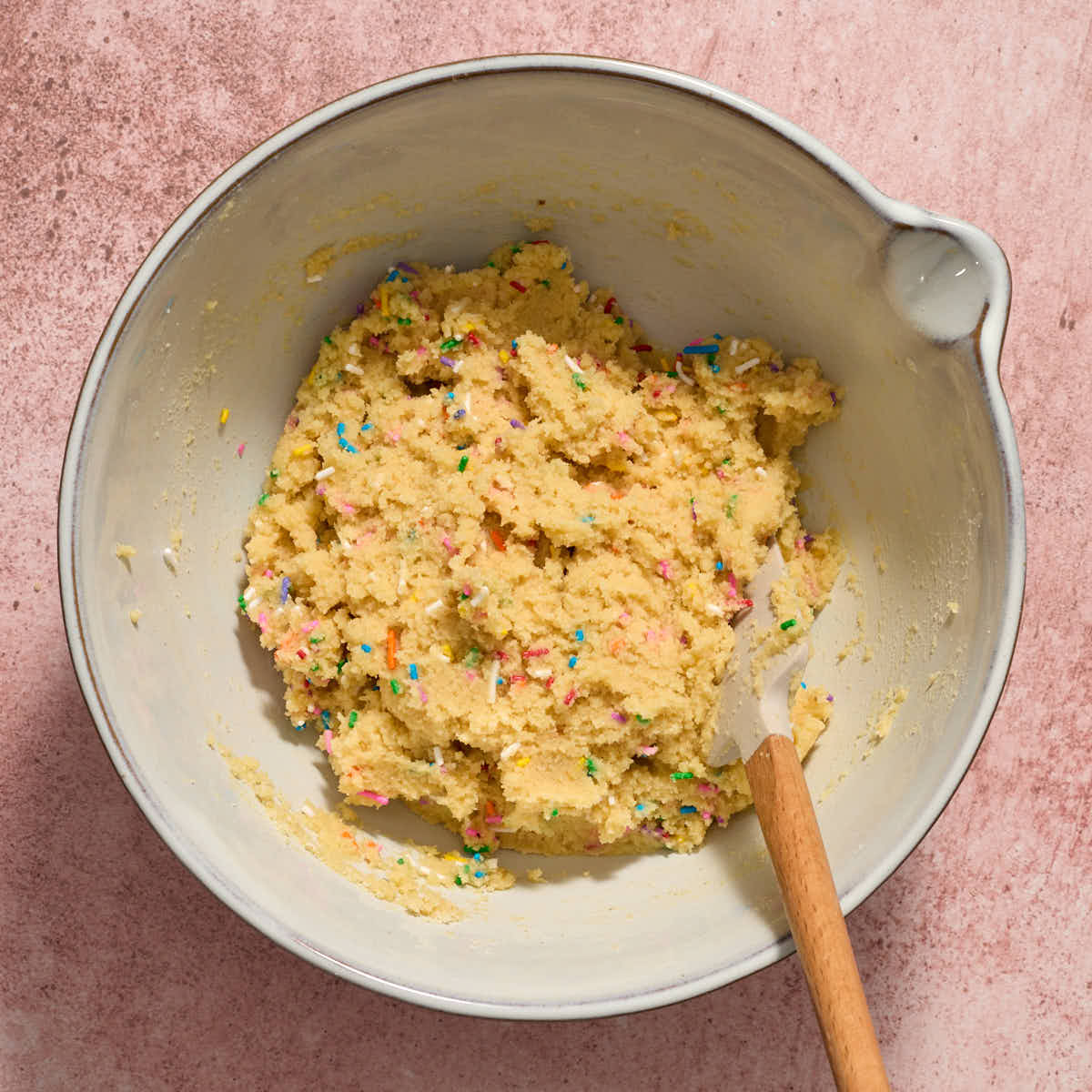 Sprinkles mixed into the cookie dough in a bowl with a spatula.