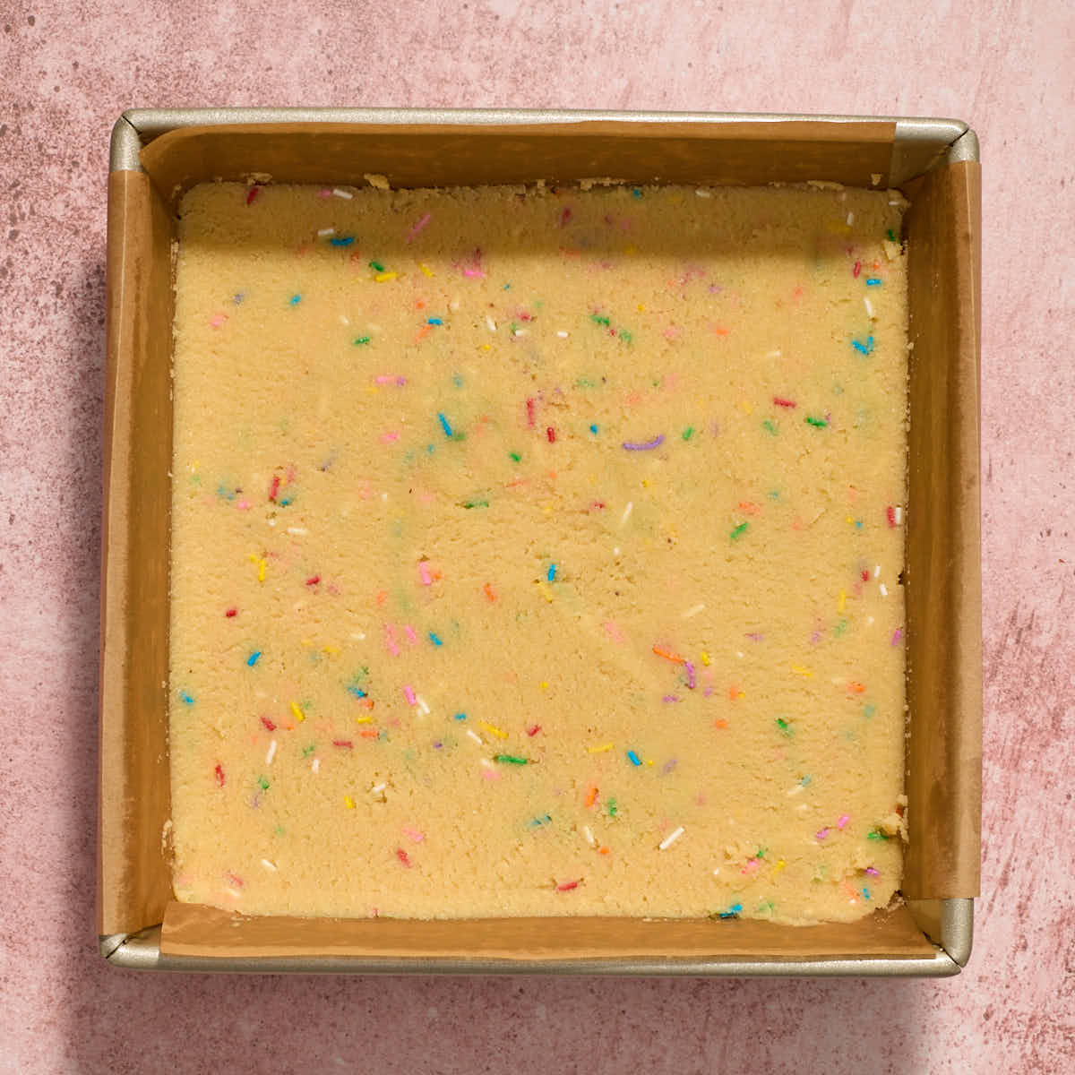 Cookie dough spread out in an 8-inch square pan.