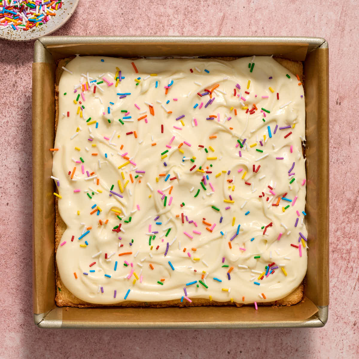 Sugar cookie bars in the pan and topped with frosting and sprinkles.