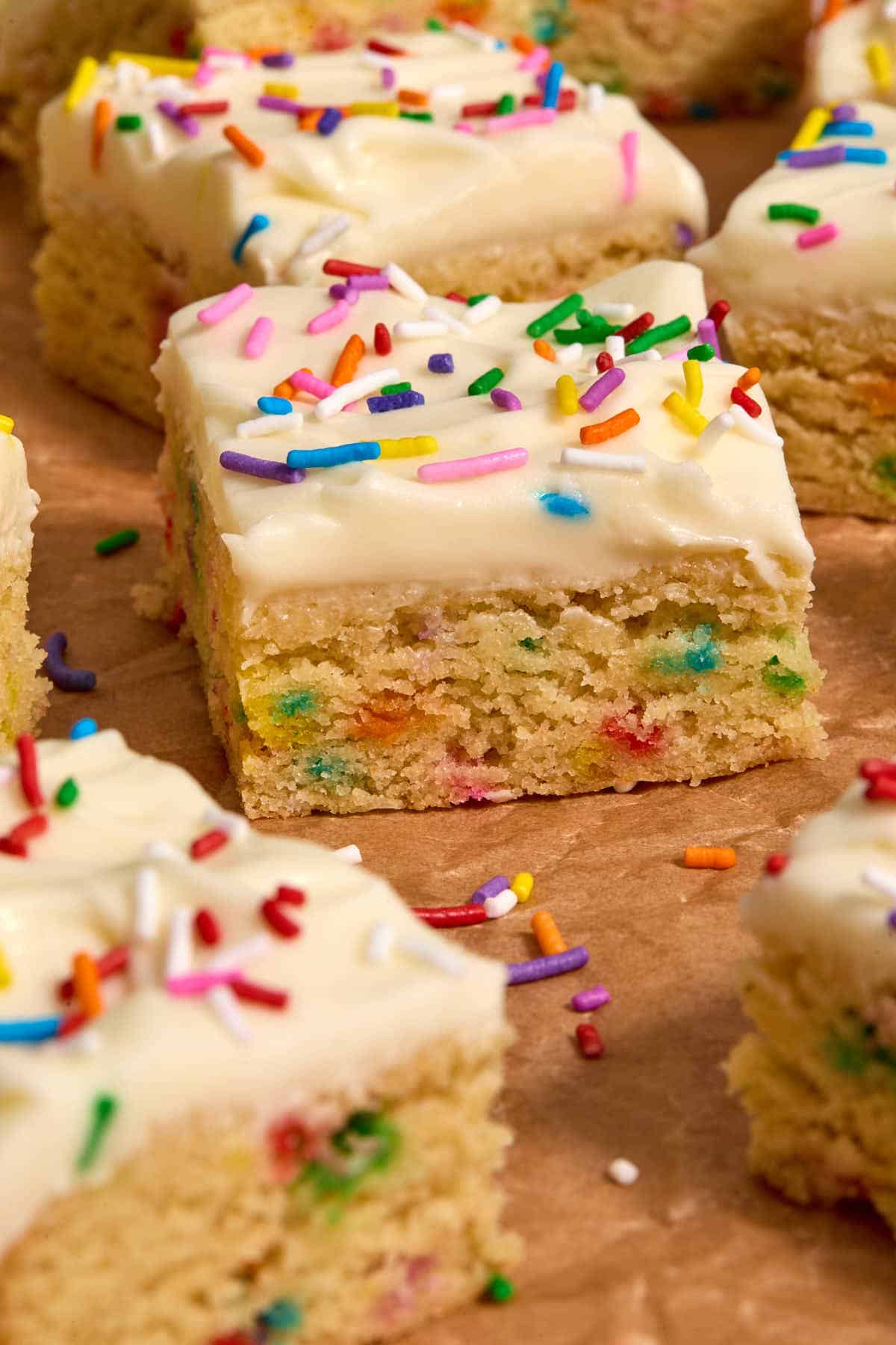 Side view of frosted sugar cookie bars arranged on brown parchment paper.