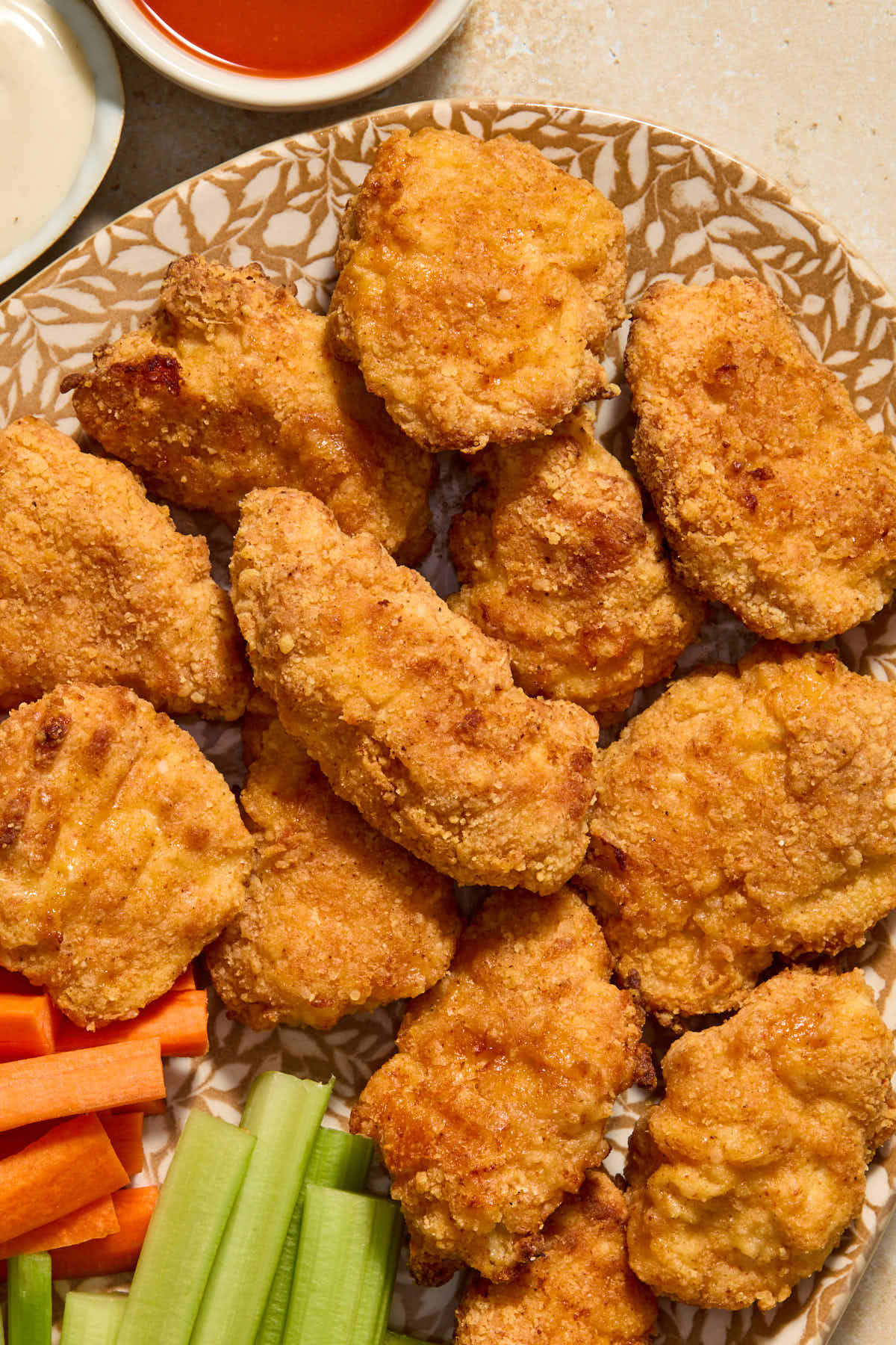 Boneless wings served on a platter with carrots and celery and dipping sauces on the side.