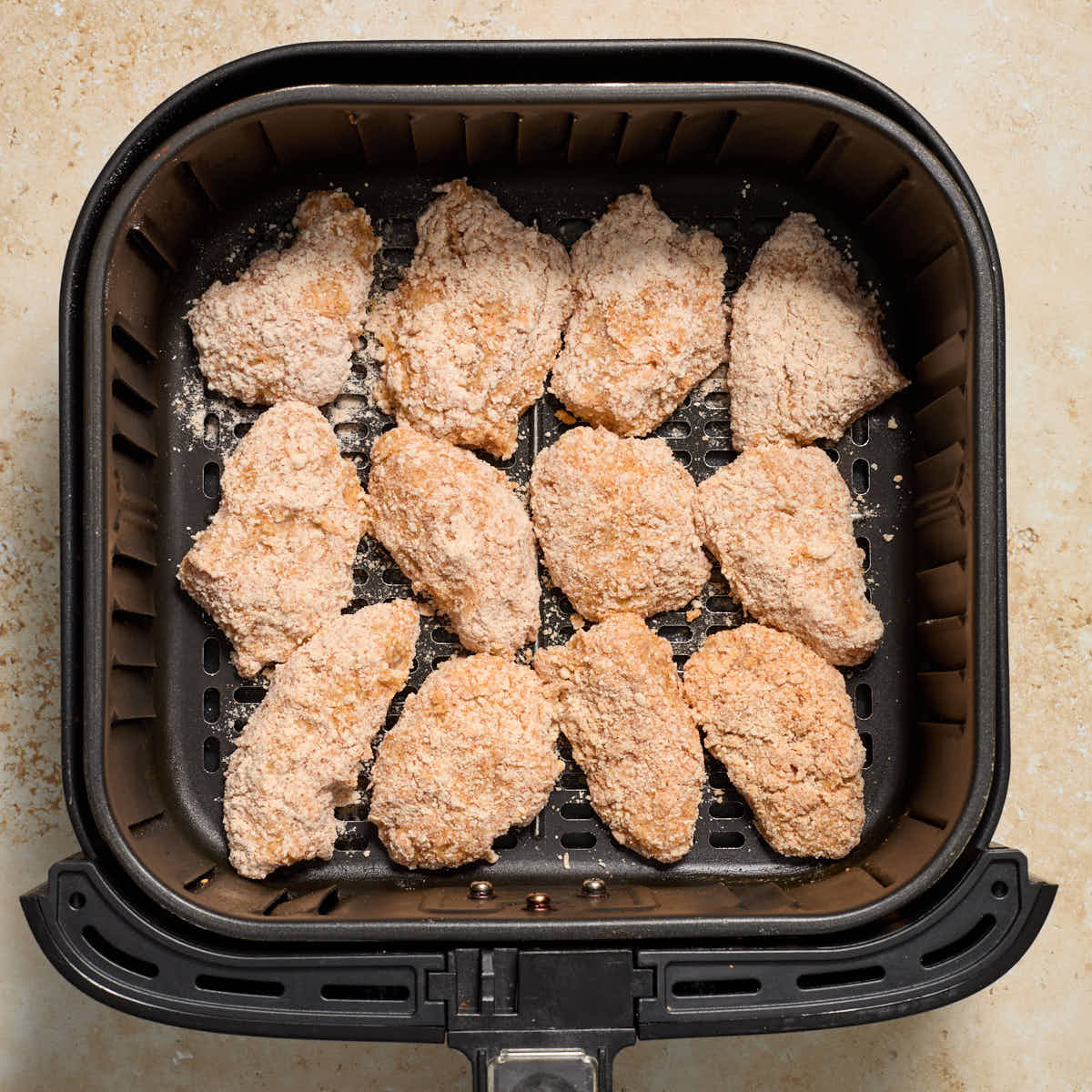 Breaded chicken pieces arranged in a single layer in an air fryer basket.
