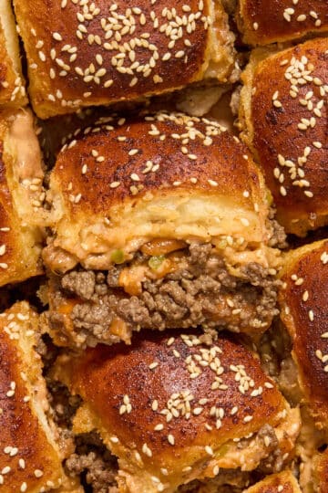 Close up of ground beef sliders with one turned on its side to show the ground beef and cheese filling.