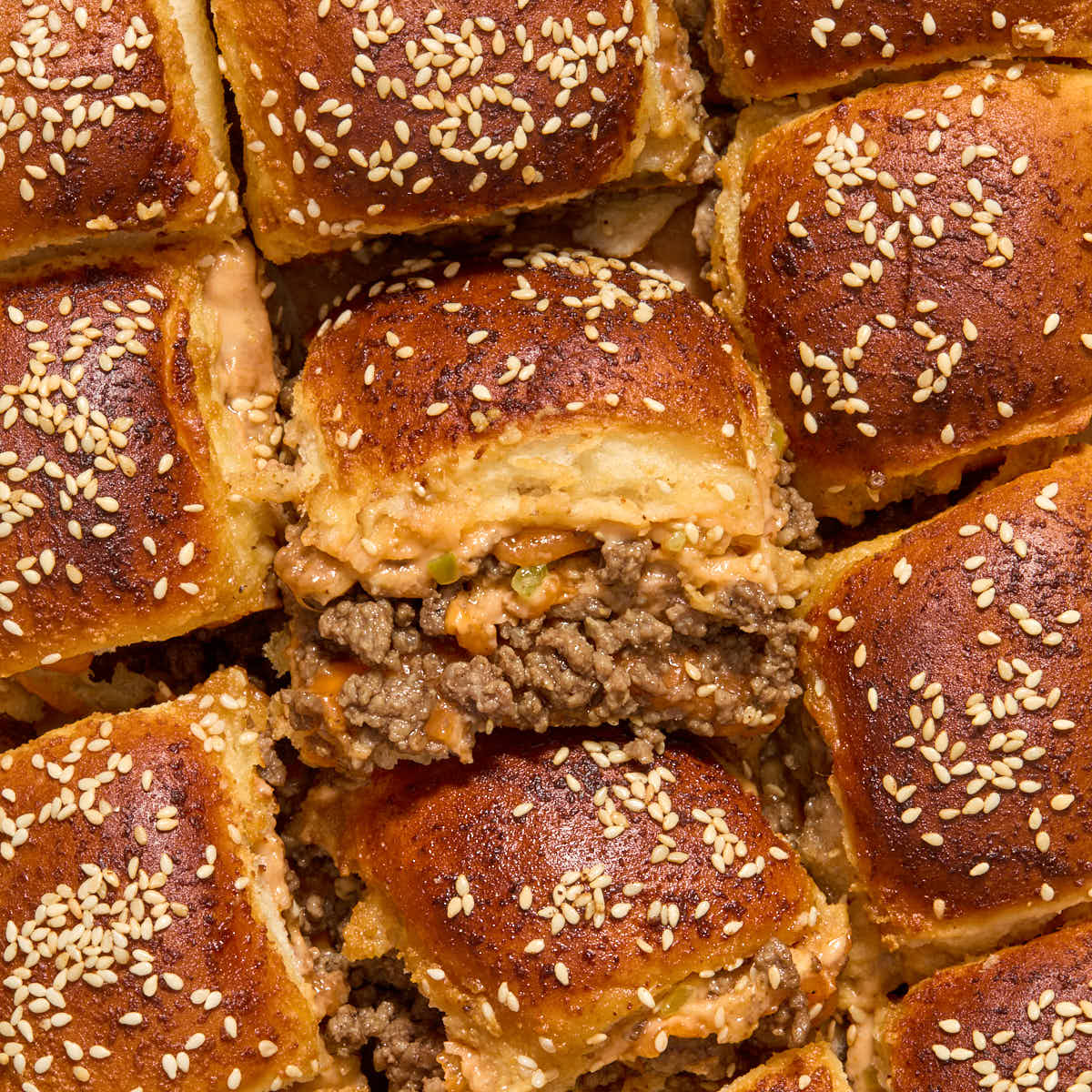 Close up of ground beef sliders with one turned on its side to show the ground beef and cheese filling.