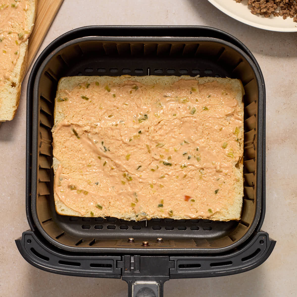 The bottom half of the sweet rolls in the air fryer basket with burger sauce spread on it.