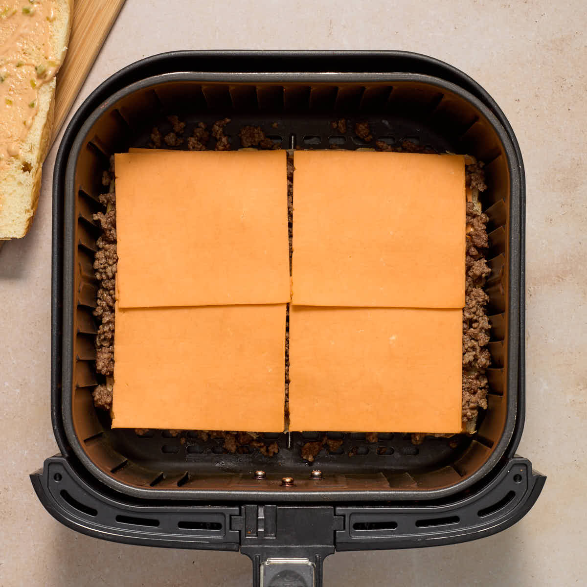 Sliced cheddar cheese, ground beef and more cheese layered on the sweet rolls in the air fryer basket.