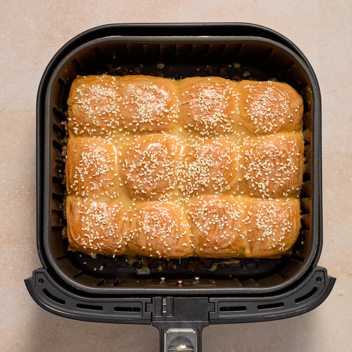 Sliders fully assembled in the air fryer basket with the melted butter mixture and sesame seeds on top.