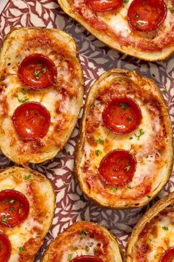 Air Fryer Pizza Potato Skins arranged on a platter and topped with chopped herbs.
