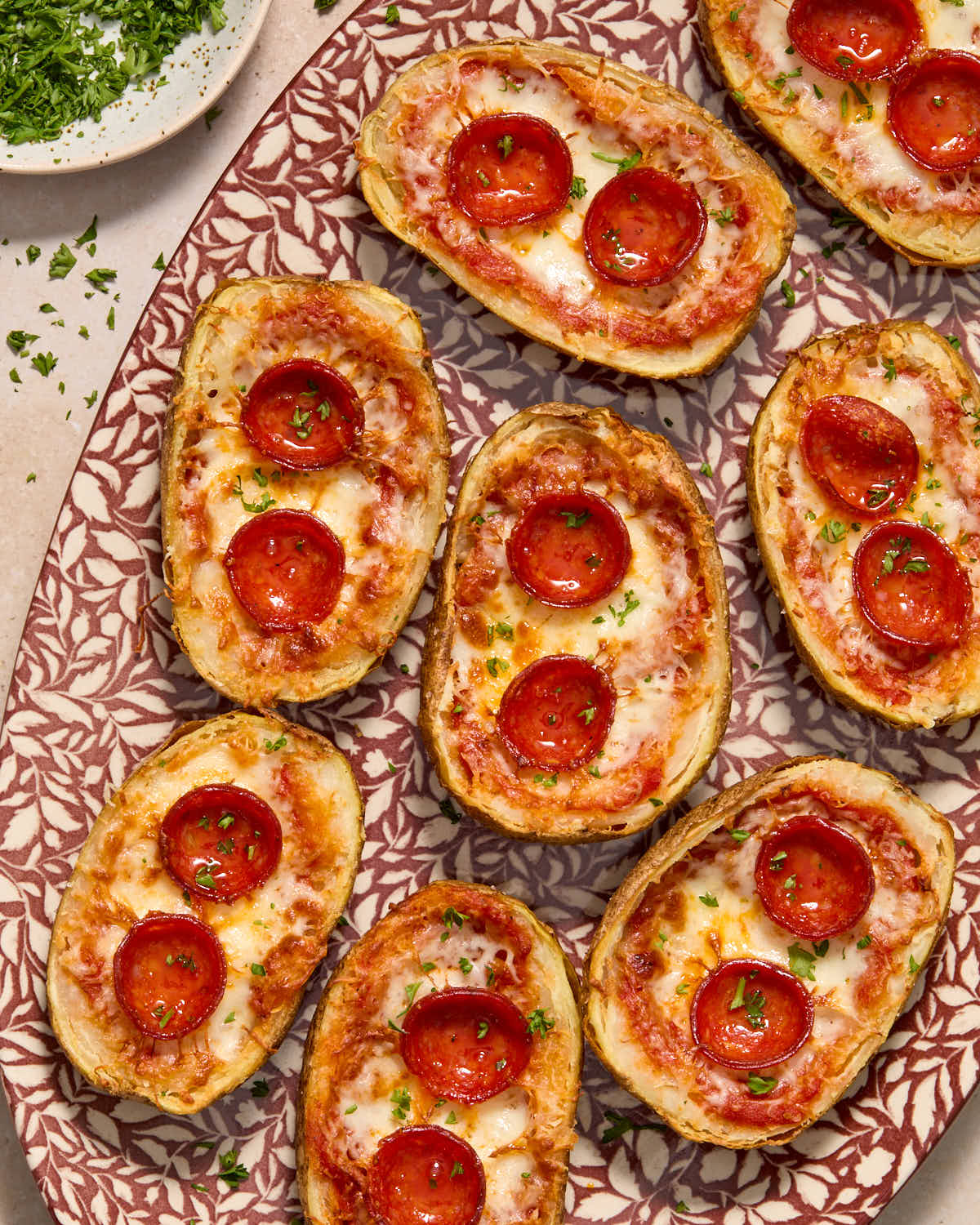 Potato skins served on a platter with chopped herbs on top and on the side.