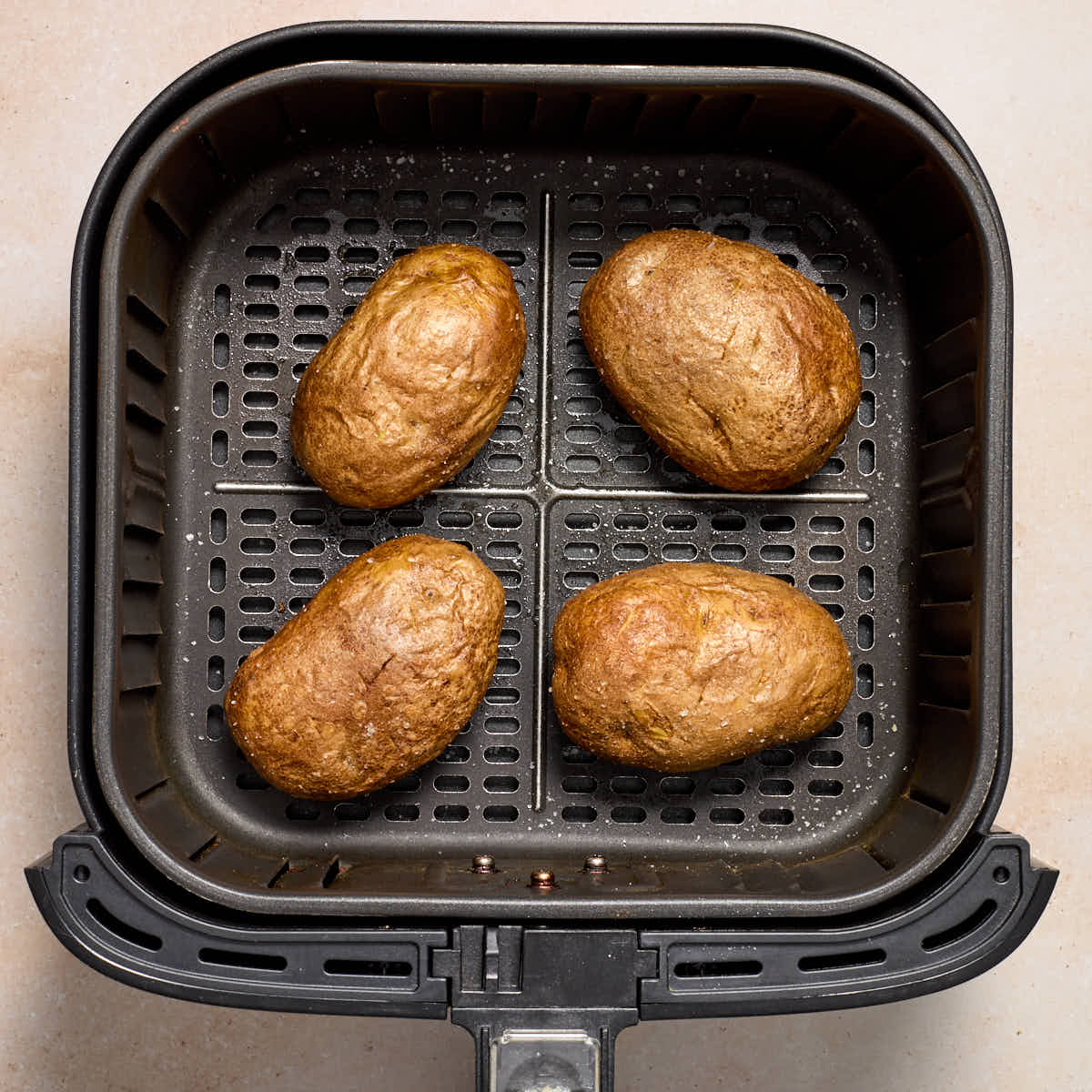 Four baked potatoes in an air fryer basket.