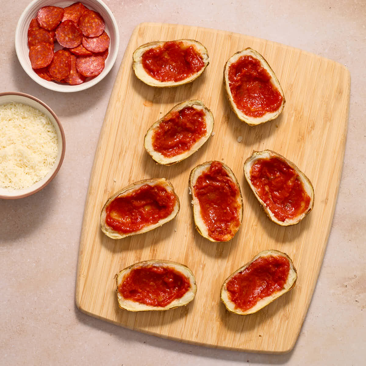 Potato skins on a wooden work surface with marinara sauce spread out in each one.