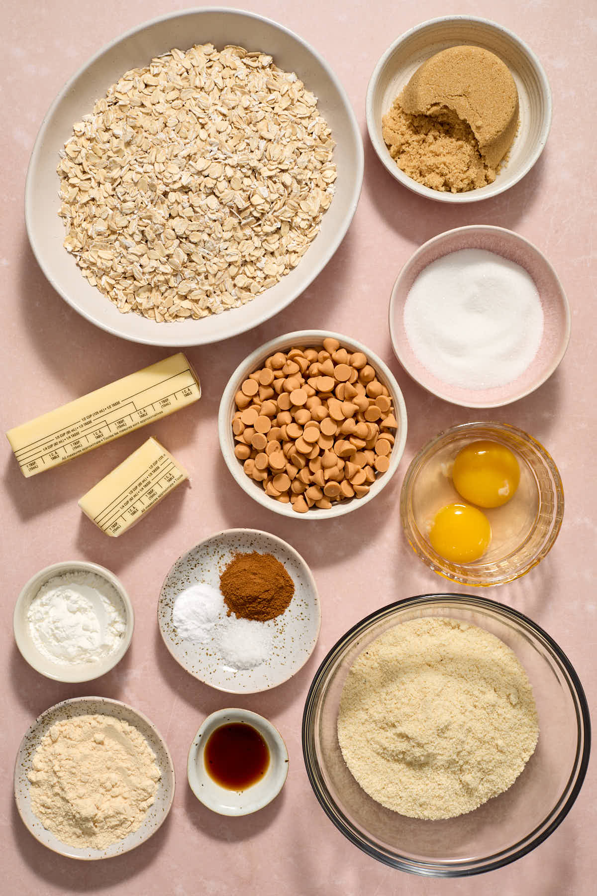 Ingredients to make almond flour oatmeal scotchies arranged individually on a pink surface.