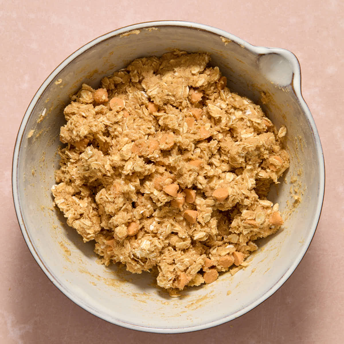 Butterscotch chips stirred into the oatmeal cookie dough in a white bowl.