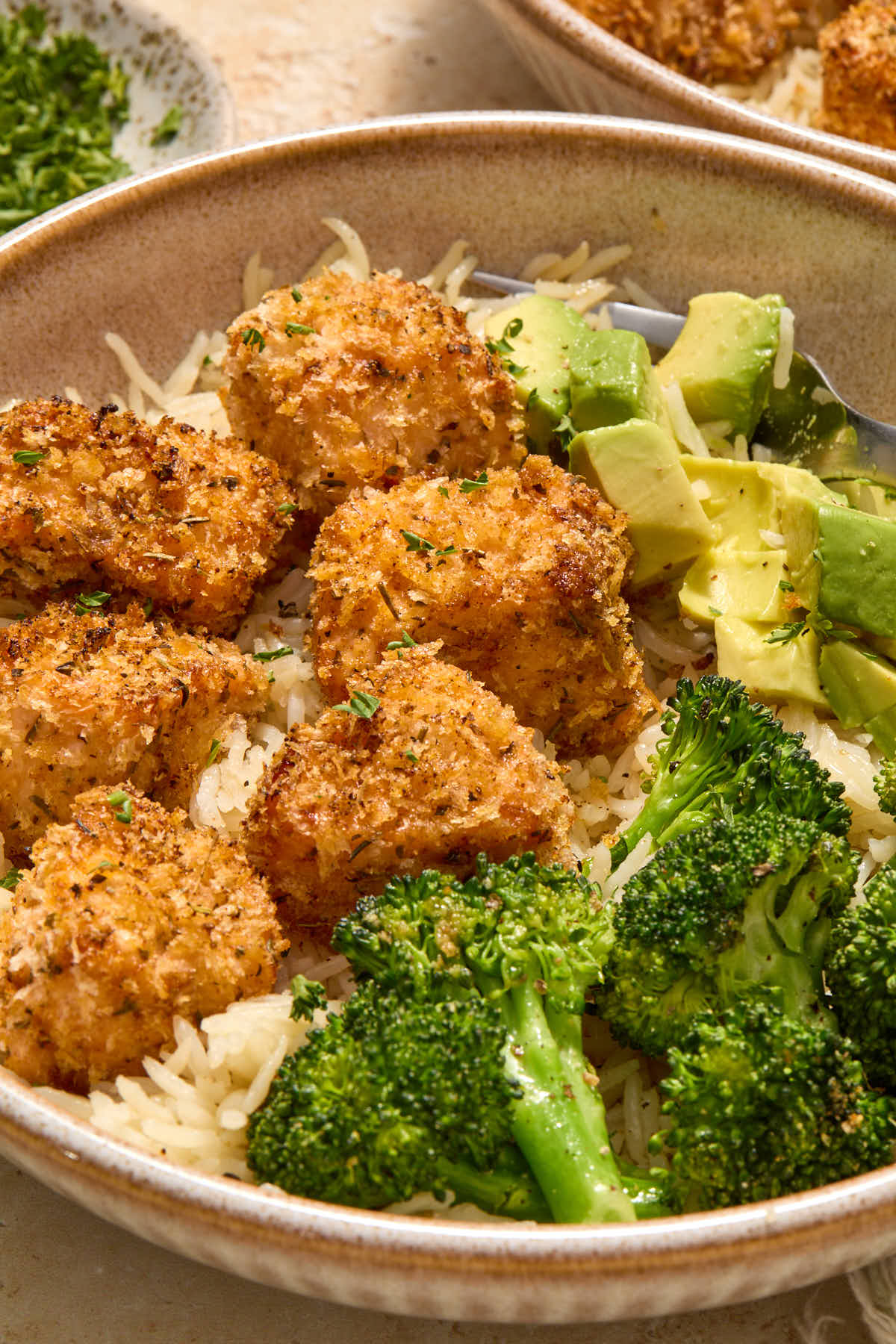 Angled close up of salmon bites in a bowl with broccoli, rice and avocado.