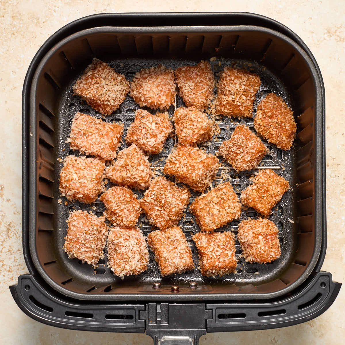 Raw breaded salmon bites in a single layer in an air fryer basket.